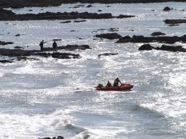 An RNLI inshore lifeboat approaching people cut off by rising waves on the rocks near Worms Head