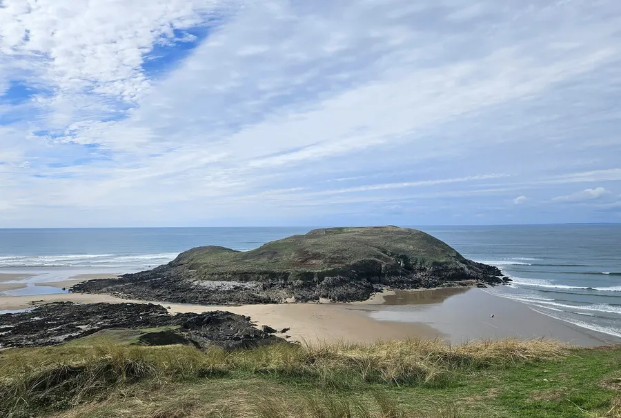 Burry Holms at low tide, seen from the grassy headland above Llangennith beach, with sand and rocks exposed around the island