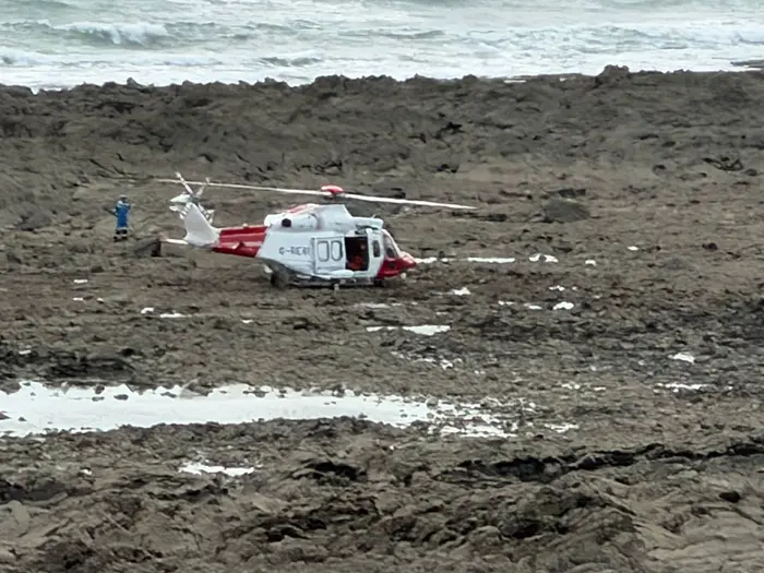 A Coastguard search and rescue helicopter landed on the rocky causeway near Worms Head, with a rescuer standing by