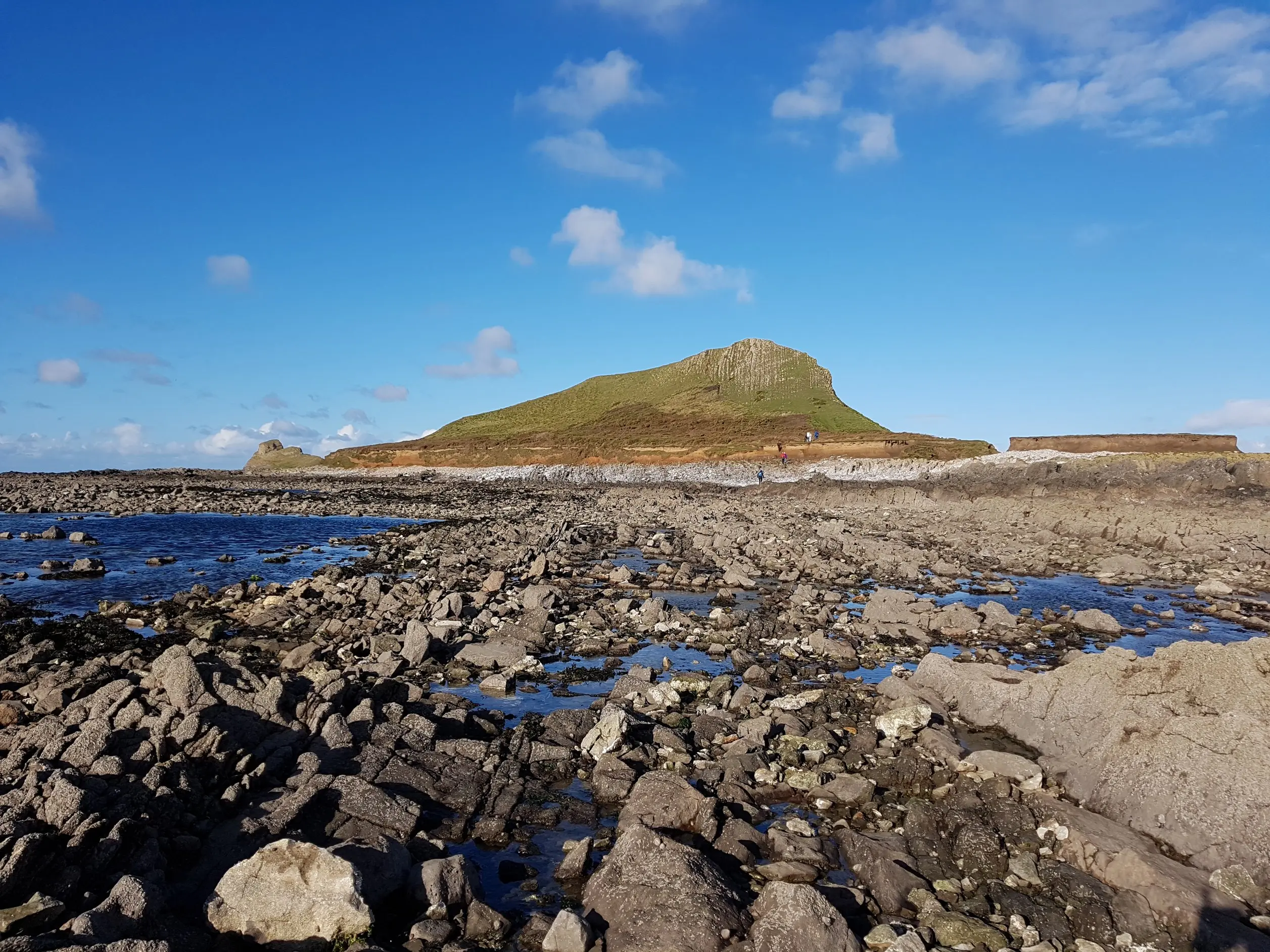 The rocky, pool-strewn causeway leading out to Inner Head at low tide, showing the uneven ground walkers have to scramble across
