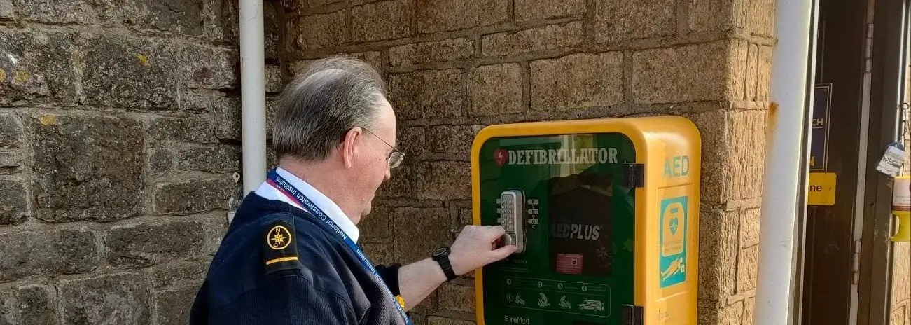 A watchkeeper opening the defibrillator (AED) cabinet mounted on the outside wall of NCI Worms Head Lookout Station