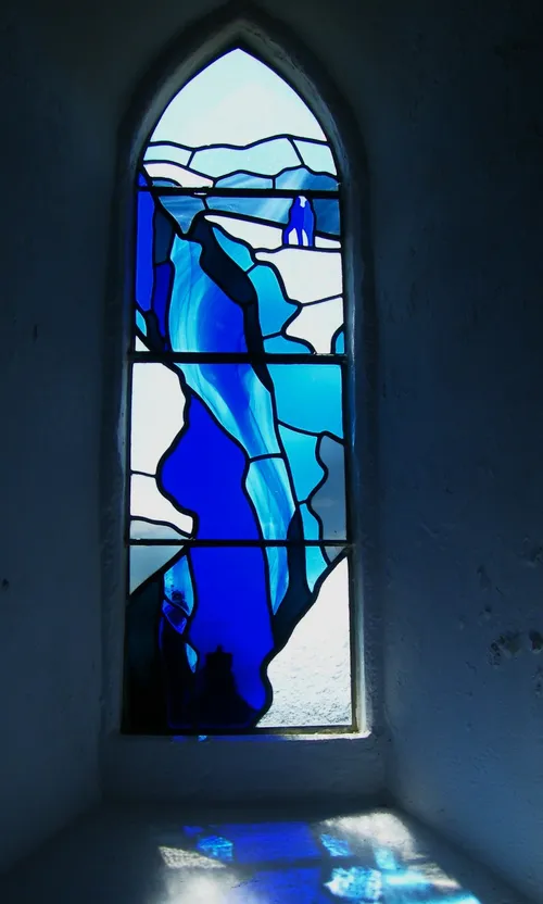 The blue stained-glass Edgar Evans memorial window in St Mary's Church, Rhosili, casting blue light onto the stone sill below