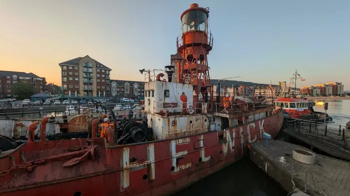 The rusted Helwick lightvessel being moved into Swansea Dry Dock at sunset, with workers on deck