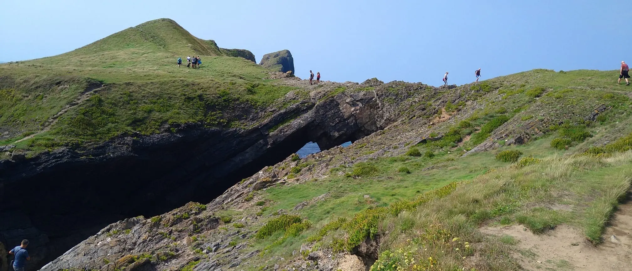 Looking up at Devil's Bridge, the natural rock arch on Worms Head, with walkers on the path above