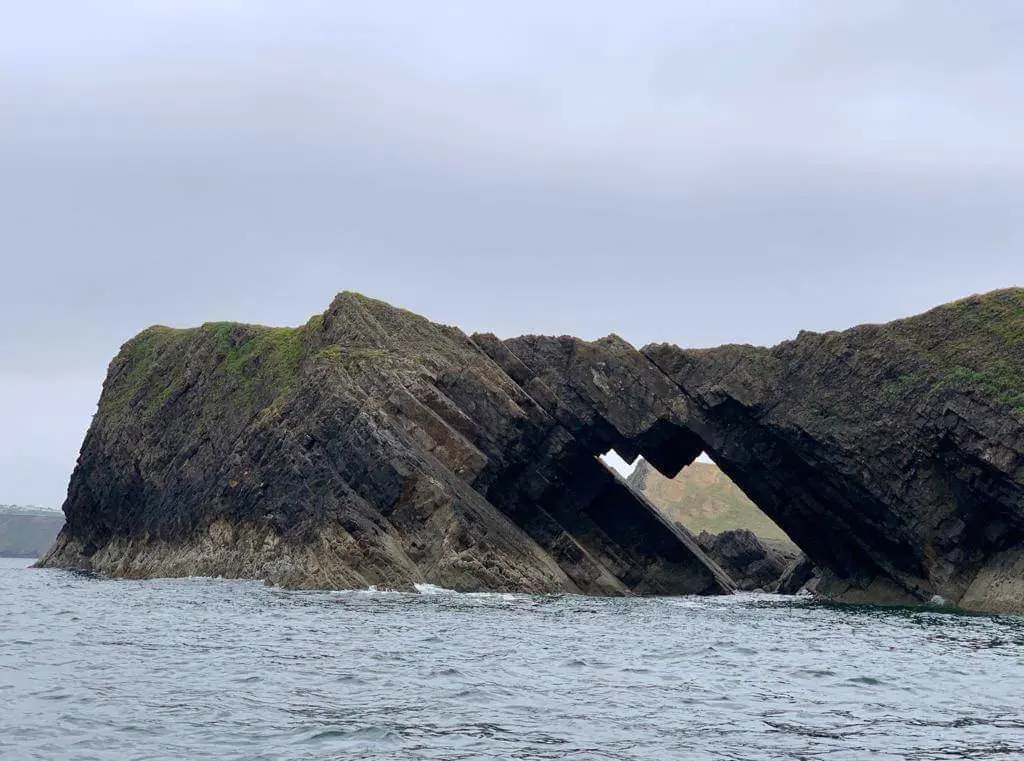 A dramatic natural rock arch on Worms Head, its tilted, layered limestone strata clearly visible from the water