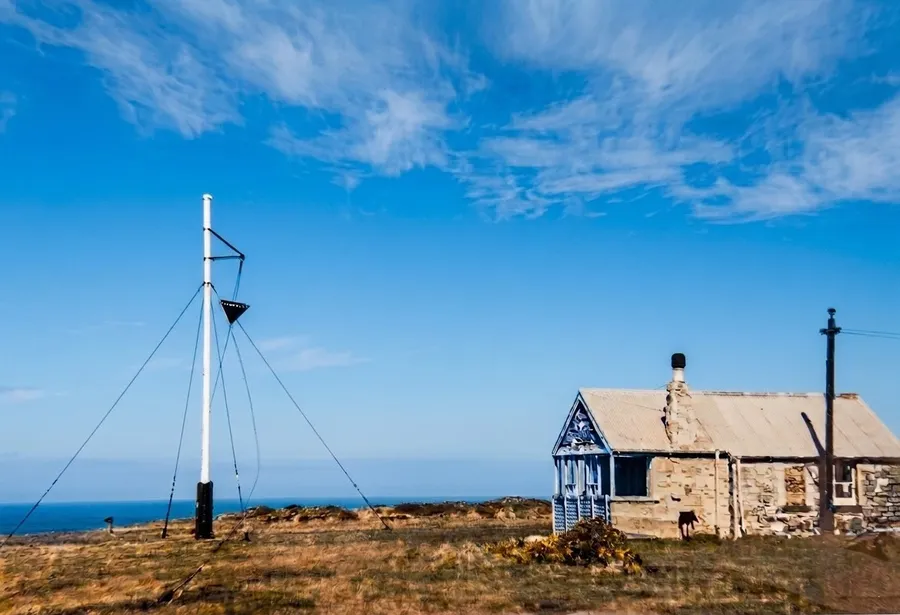 Historic photograph of the old Coastguard lookout at Rhosili, with the weather mast beside it flying a storm cone