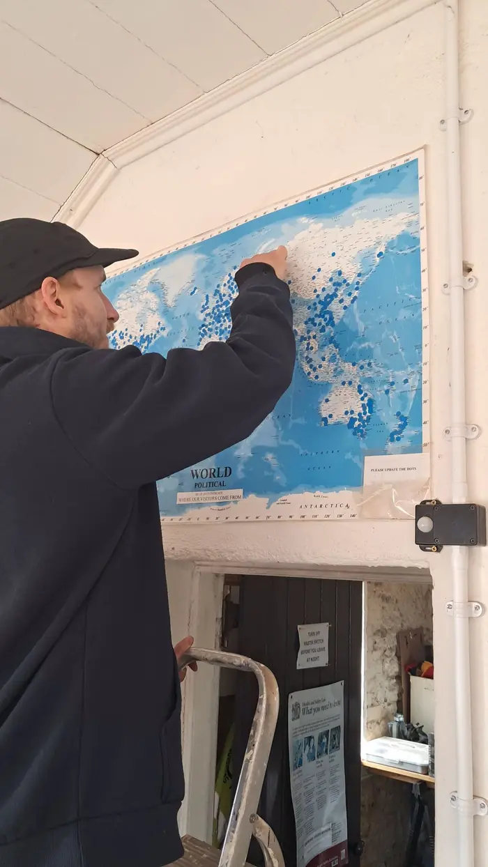 A watchkeeper on a stepladder adding a new blue dot to the world visitors map
