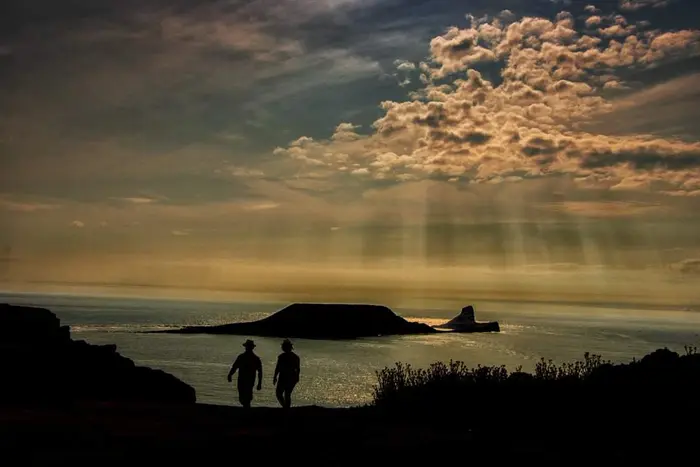 Walkers silhouetted on the clifftop at sunset, with the Worm beyond
