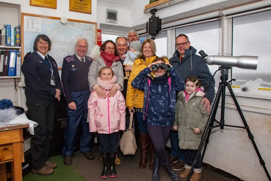 A visiting family with two NCI watchkeepers in the watch room, one of the children trying out the binoculars