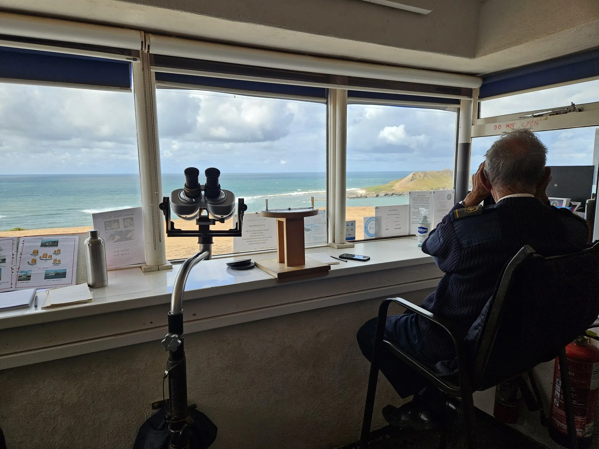 A watchkeeper scanning Worms Head through binoculars from the lookout's watch room