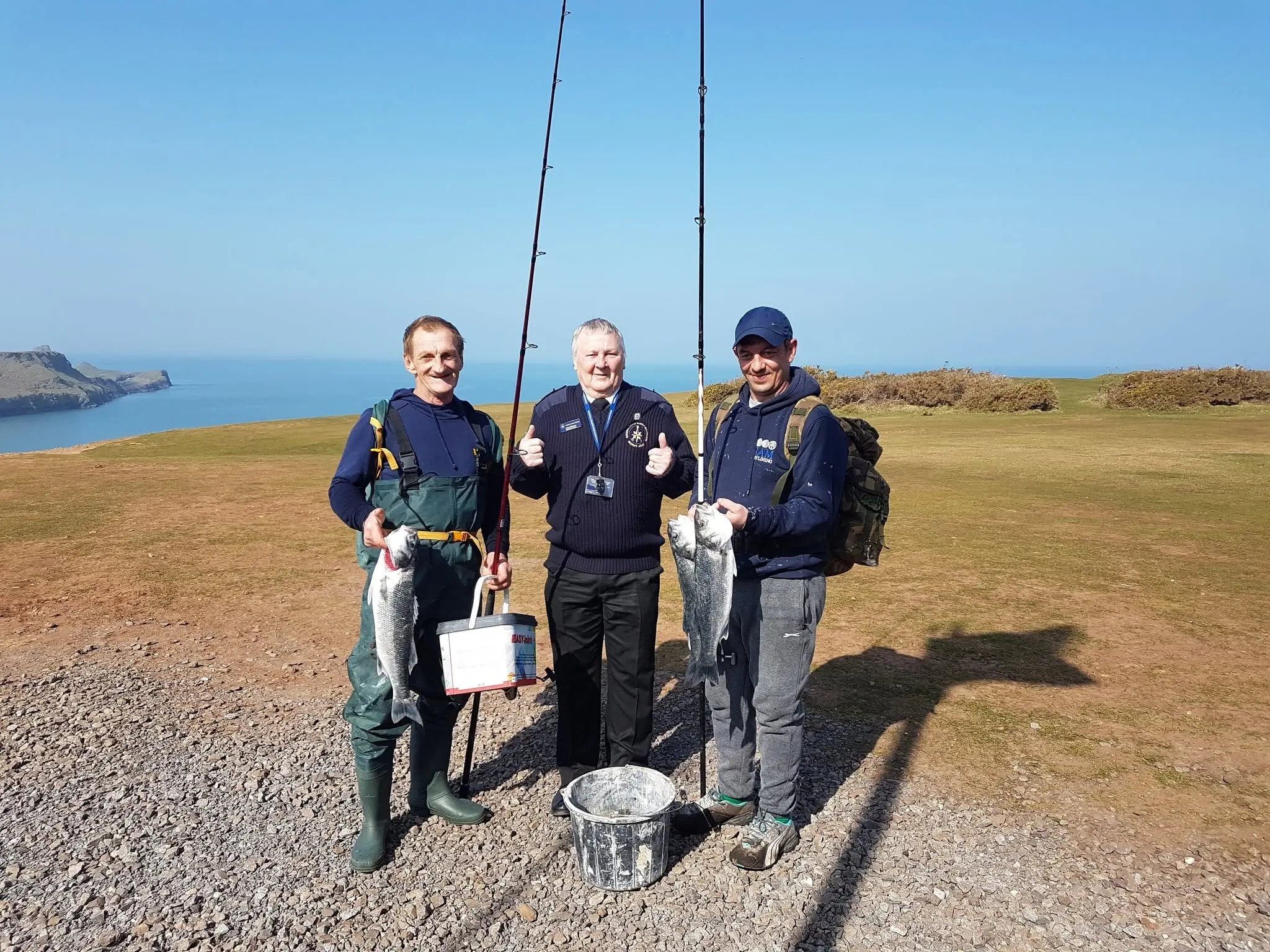 An NCI Worms Head watchkeeper with two local anglers and their catch on the clifftop above Worms Head