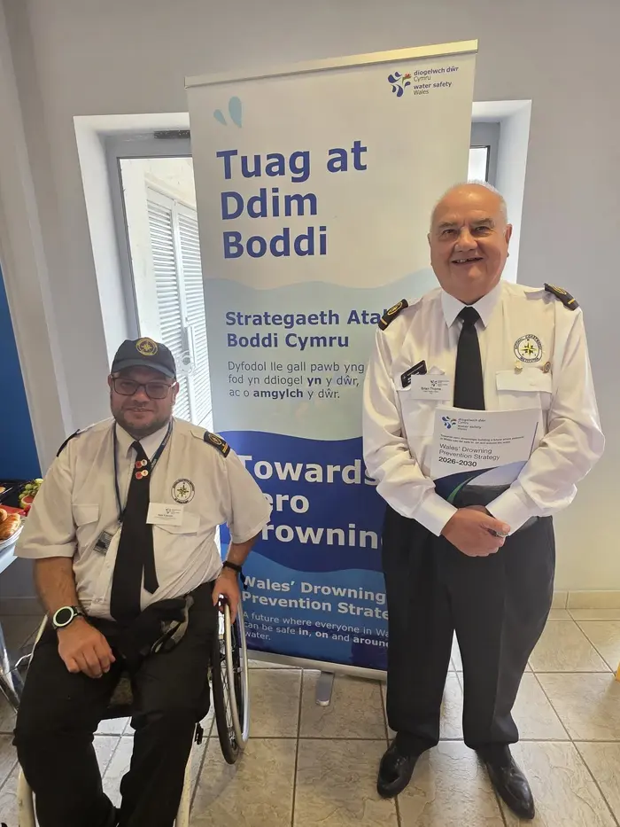 Station manager Neil and coastal water safety lead Brian in NCI uniform beside a Water Safety Wales ‘Towards Zero Drownings’ banner