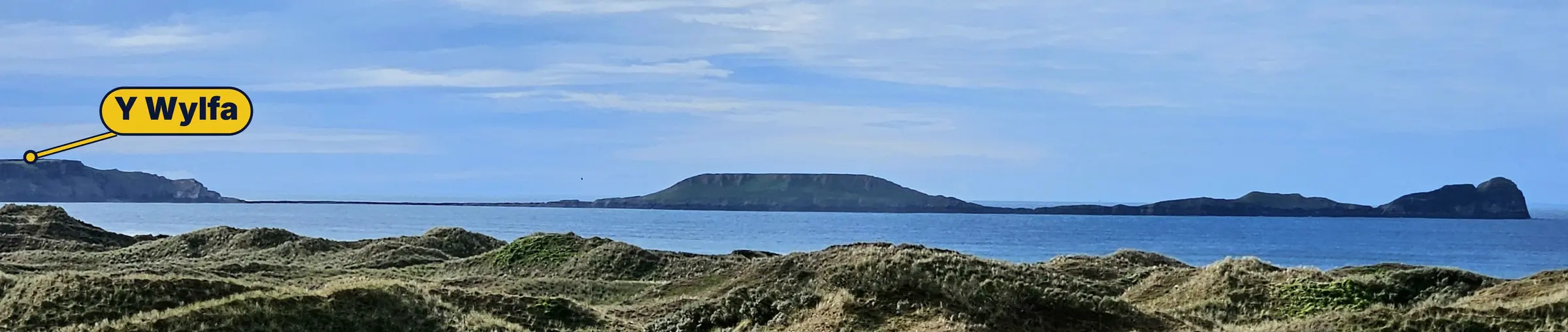 Pen Pyrod yn ymestyn allan i'r môr, i'w weld dros dwyni tywod glaswelltog Bae Rhosili, gyda gwylfa'r NCI wedi'i nodi ar y pentir ar y chwith